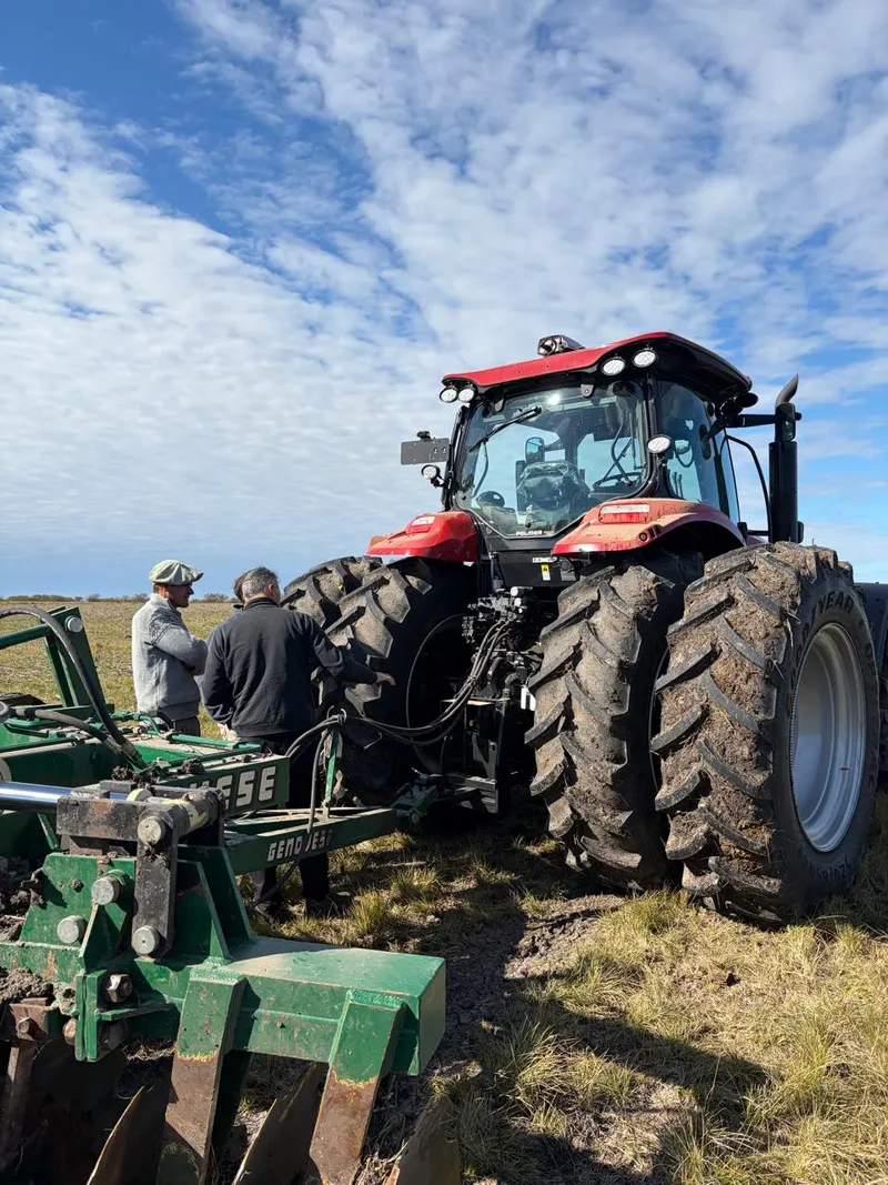 Dos operarios trabajando sobre el enganche de un implemento a un tractor, en el campo